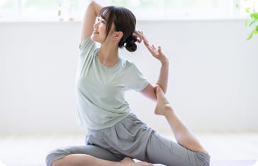 明るい室内で、女性がヨガのストレッチポーズをとっている