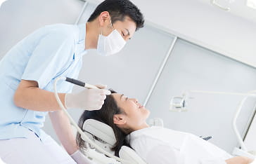 歯科医院で、マスクを着けた歯科医師が患者の口元を治療している