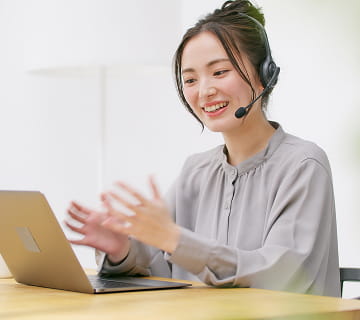 ヘッドセットをつけた女性が、ノートパソコンの前で笑顔で話している